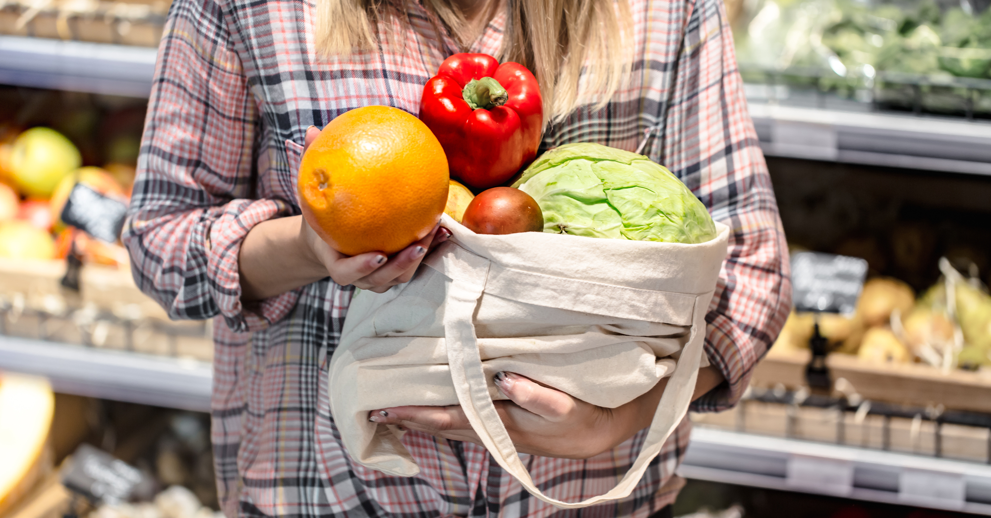 Young girl holding fruits and vegetables in an eco bag on the background of the store