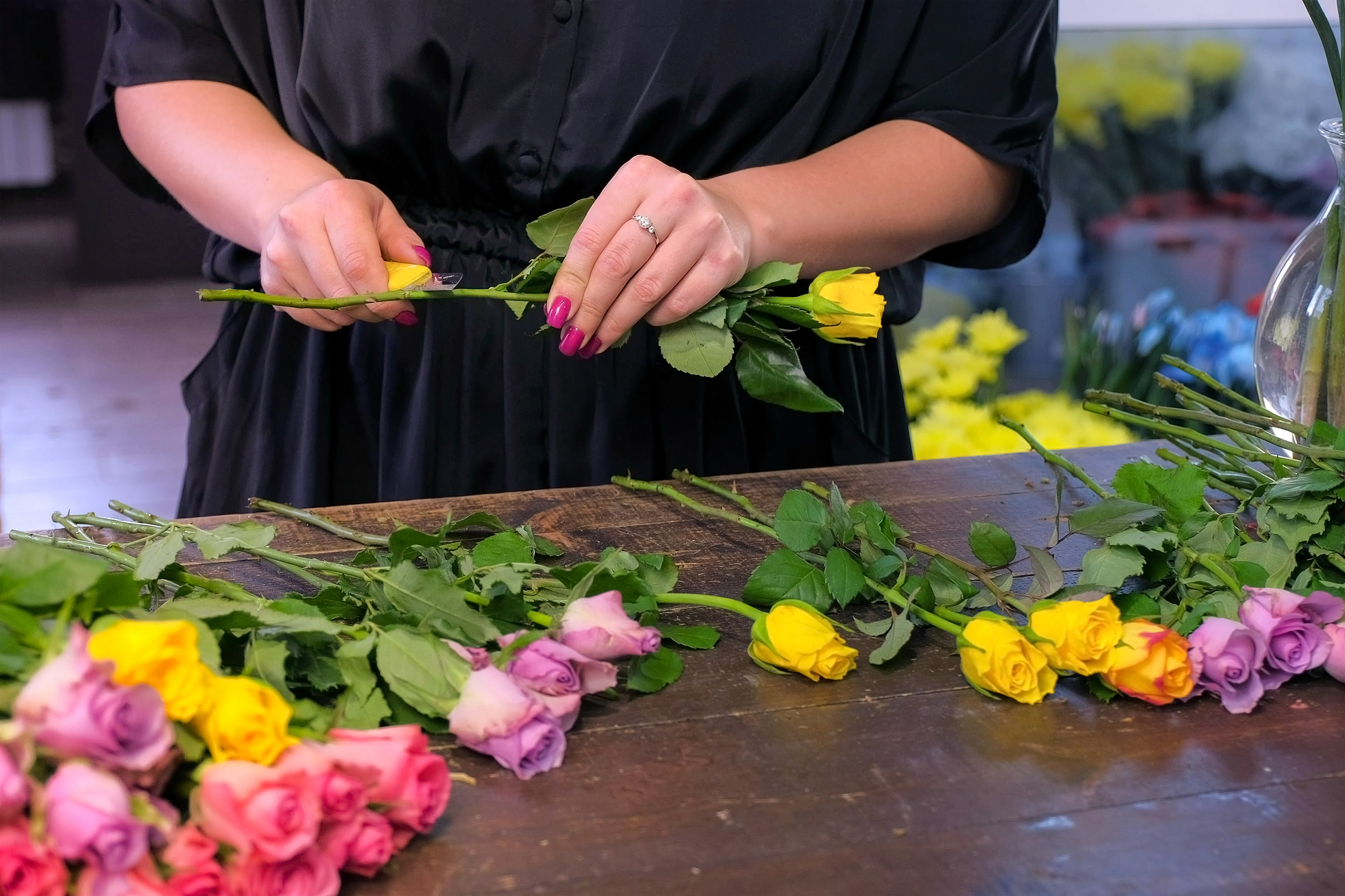 Floral business concept. Professional florist woman prepares flowers to bunch bouquet. She cuts rose thorns in shop, closeup hands. Working day in floristic studo store salon.