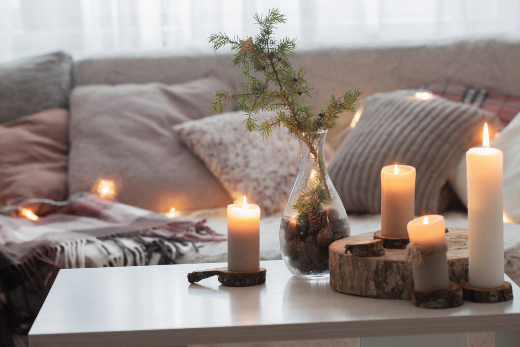 candles on white table against the background of sofa with plaids and pillows. Cozy home concept