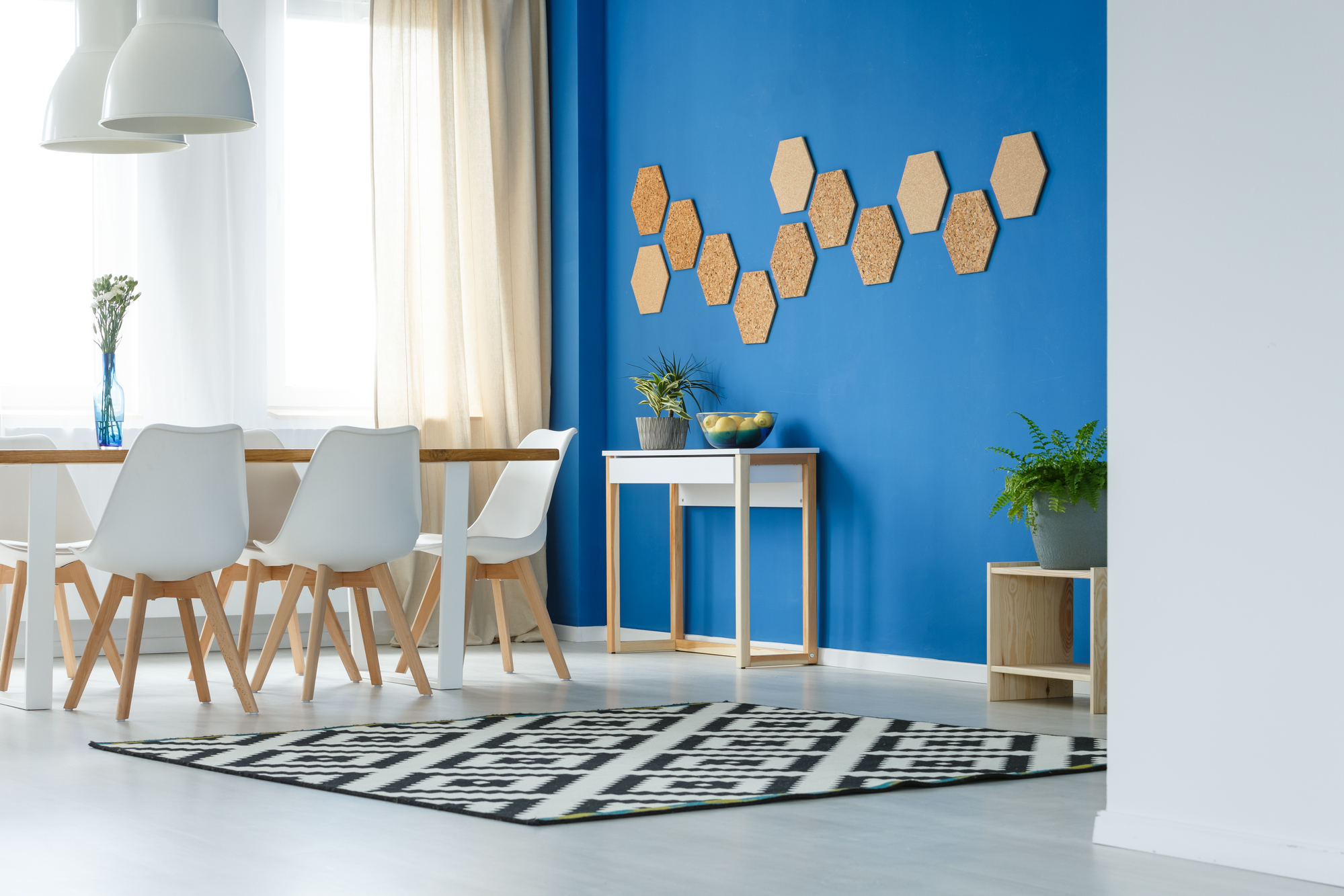 Cork honeycombs on blue wall of trendsetting dining room interior with patterned carpet, plants and white furniture