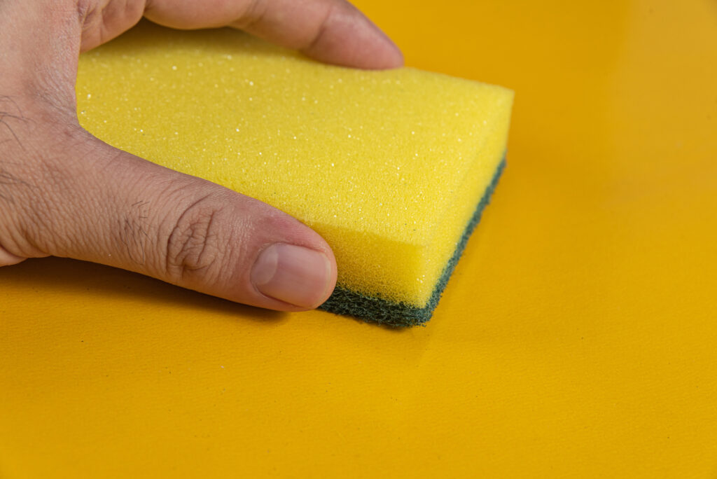 Man holding kitchen sponge on the yellow background