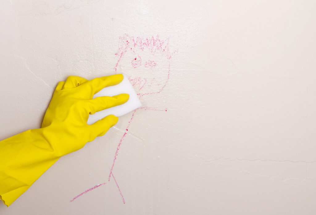 Gloved hand, cleaning crayon off wall with magic eraser