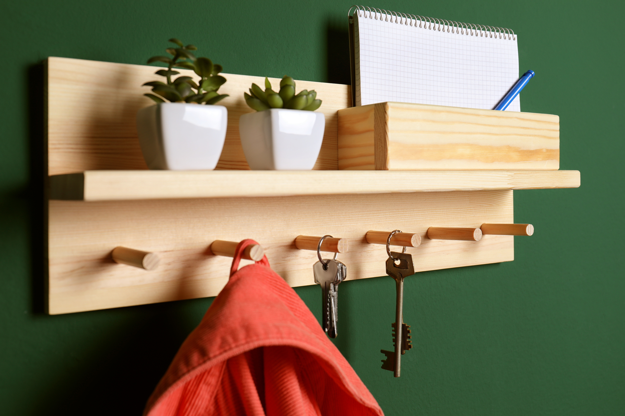 Wooden hanger for keys with clothes on green wall, closeup