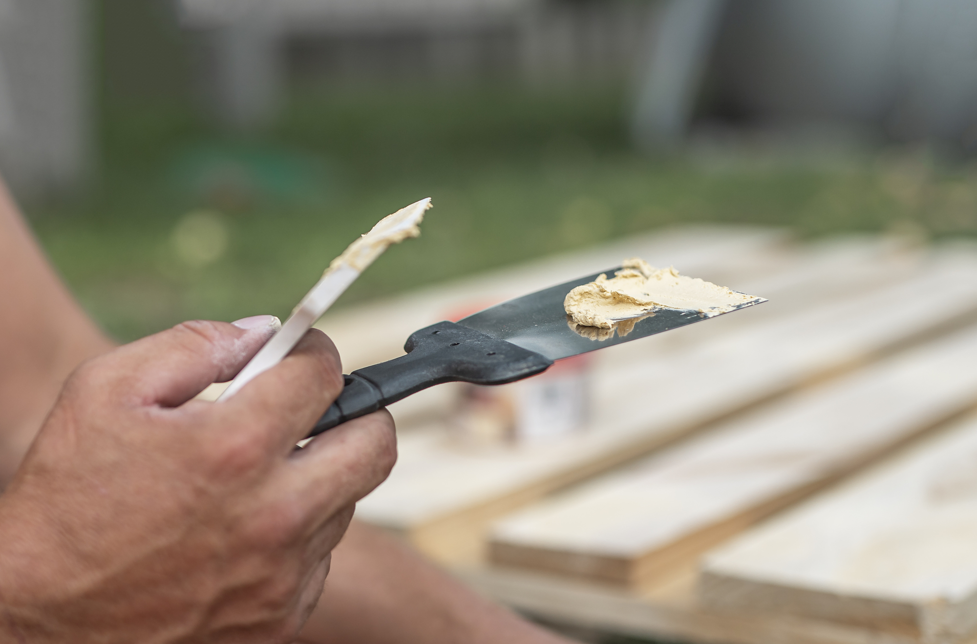 Putty on spatula tool in male hands closeup, repairing wood with paste.