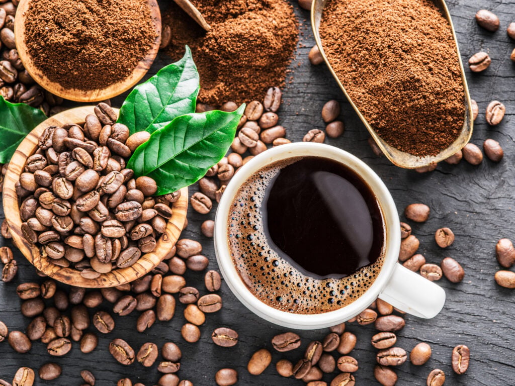 Roasted coffee beans, ground coffee and cup of coffee on wooden table. Top view.