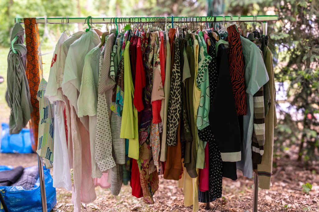 Bright and light summer shirts and blouses in pastel tones on metal rack under trees during eco event