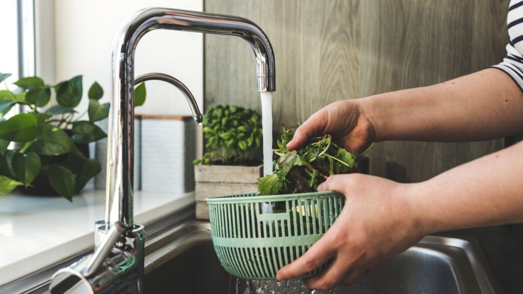 woman washing green salad under kitchen sink