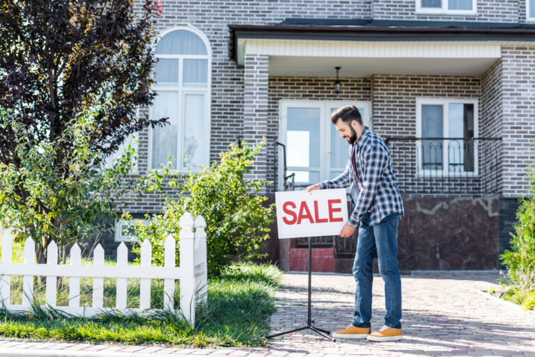 man putting for sale sign outside house