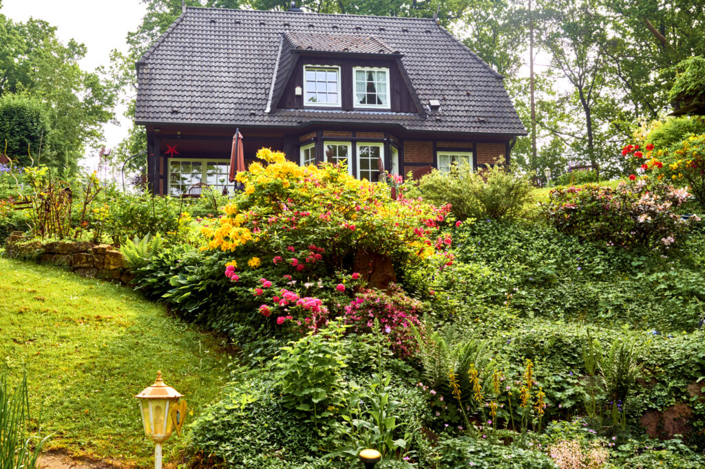 Well-kept garden with flowering shrubs , hedge and bushes in front of a large luxury family house