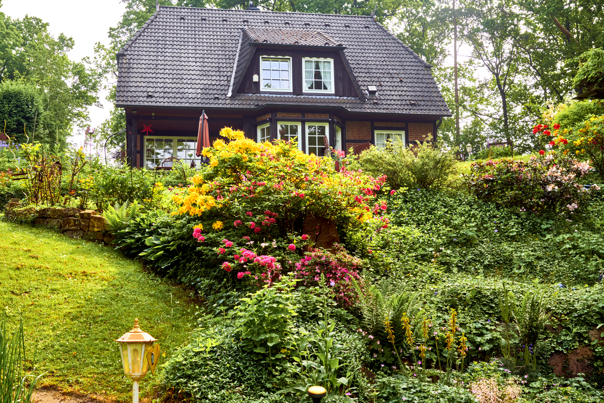 Well-kept garden with flowering shrubs , hedge and bushes in front of a large luxury family house