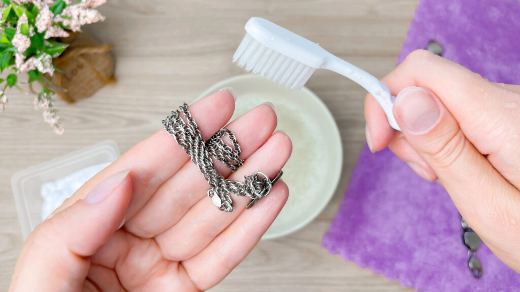 person using toothbrush to clean jewelry