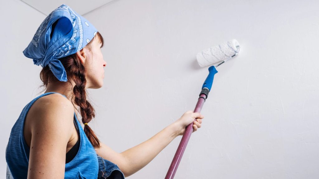 The girl in blue clothes pours paint roller white wall in the room.