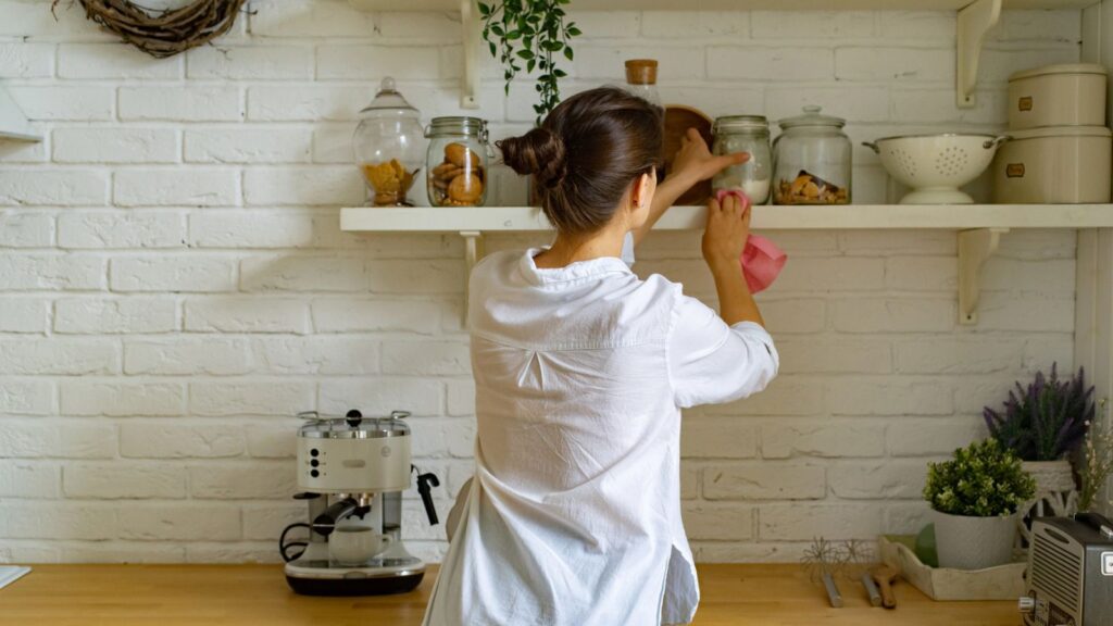 woman dusting shelves in kitchen