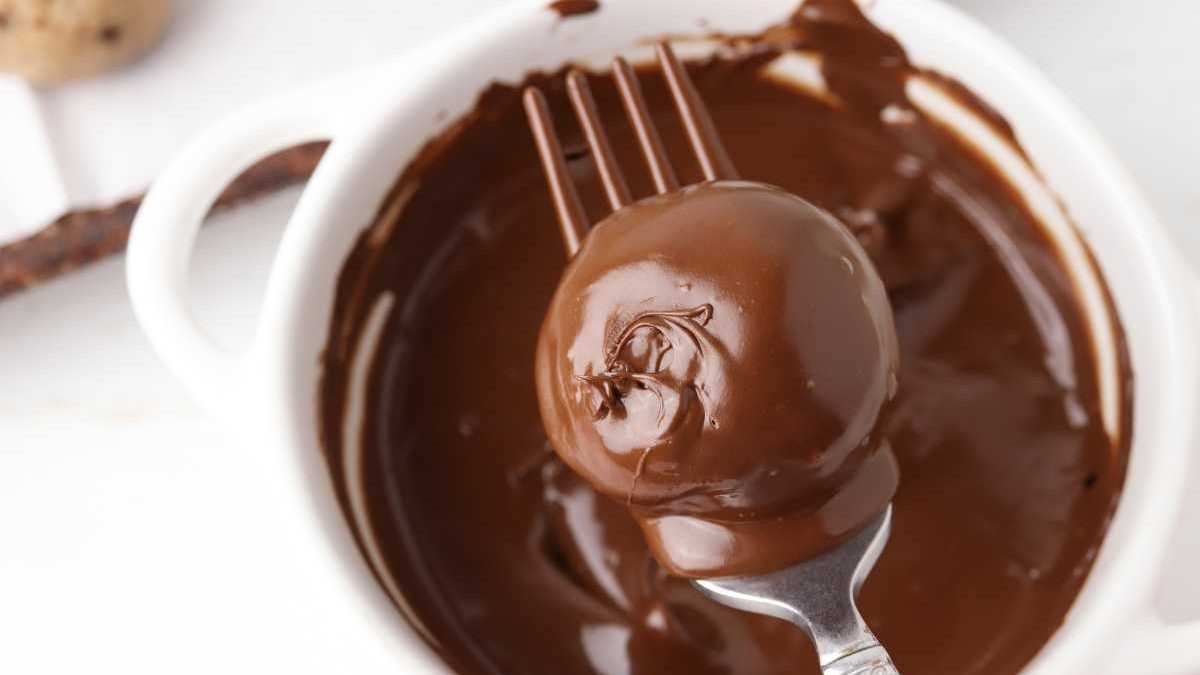A fork with chocolate sauce in a white bowl filled with Cookie Dough Balls.