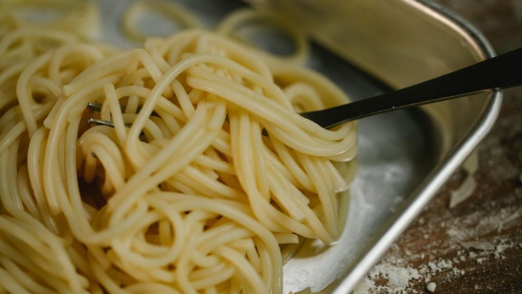 Cooked spaghetti and fork placed in steel bowl