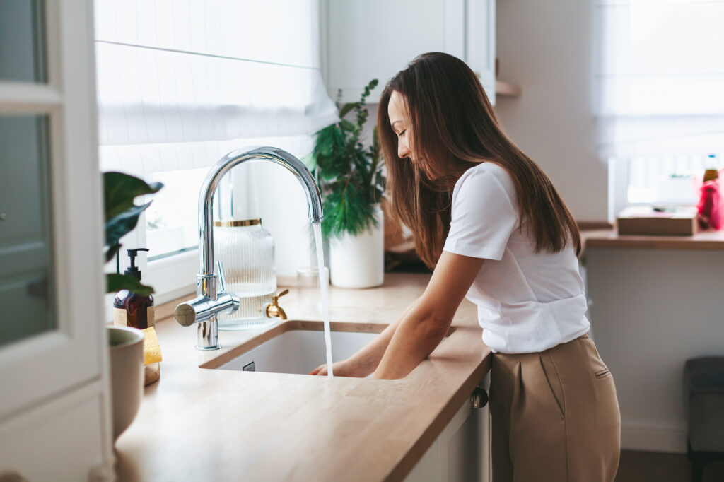 Young woman washing the dishes in the white kitchen at home