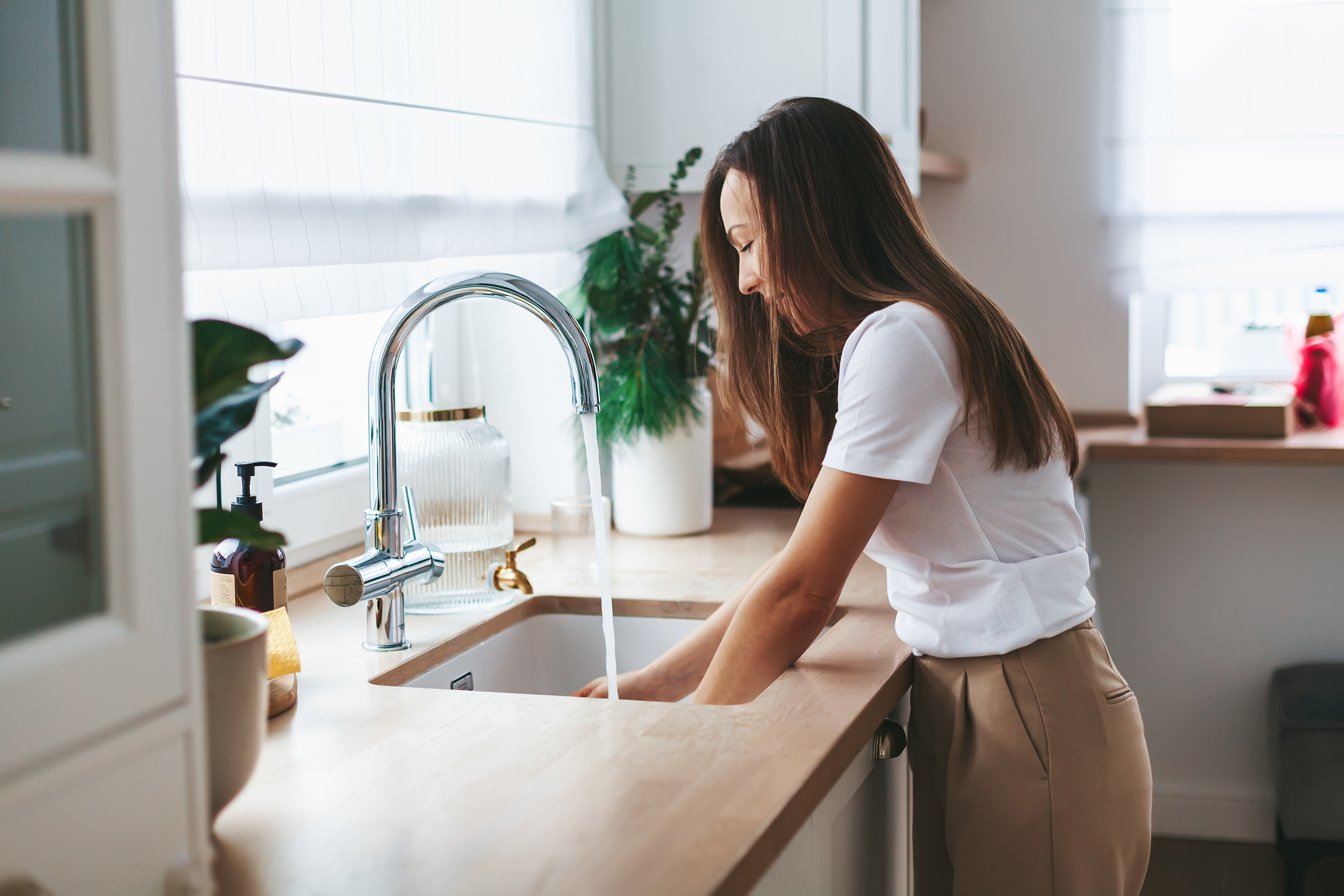 Young woman washing the dishes in the white kitchen at home