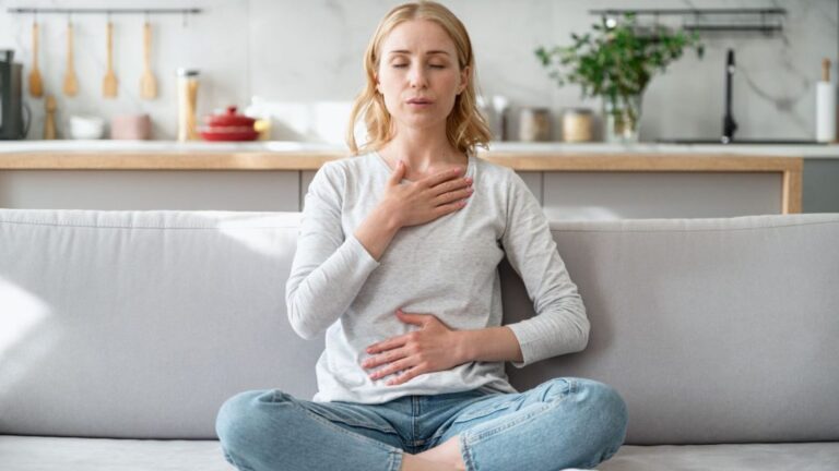 Concept of mental health. Woman sitting on couch and doing calming breathing exercises after panic attack. Female inhaling and exhaling to deep breath. Self-control, anxiety relief concept.