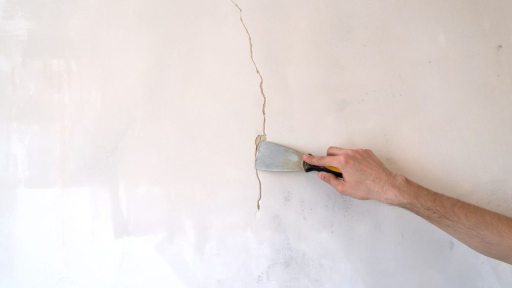 Construction man worker repairing a crack wall of a home, plastering cement on wall. Builder applying white cement to a crack in a wall with a putty knife.