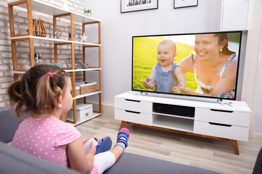 Close-up Of Innocent Girl Sitting On Sofa Watching Television In Living Room