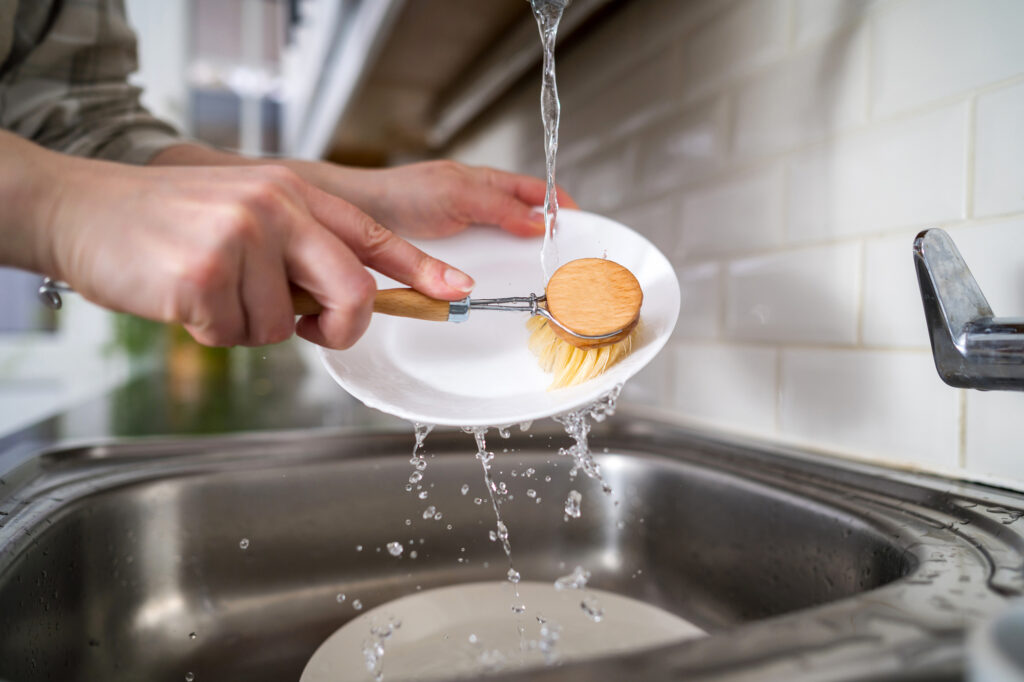 Zero waste concept. Eco-friendly kitchen wooden brush. Woman washing dishes with bamboo brush. Waste-free, eco-friendly concept